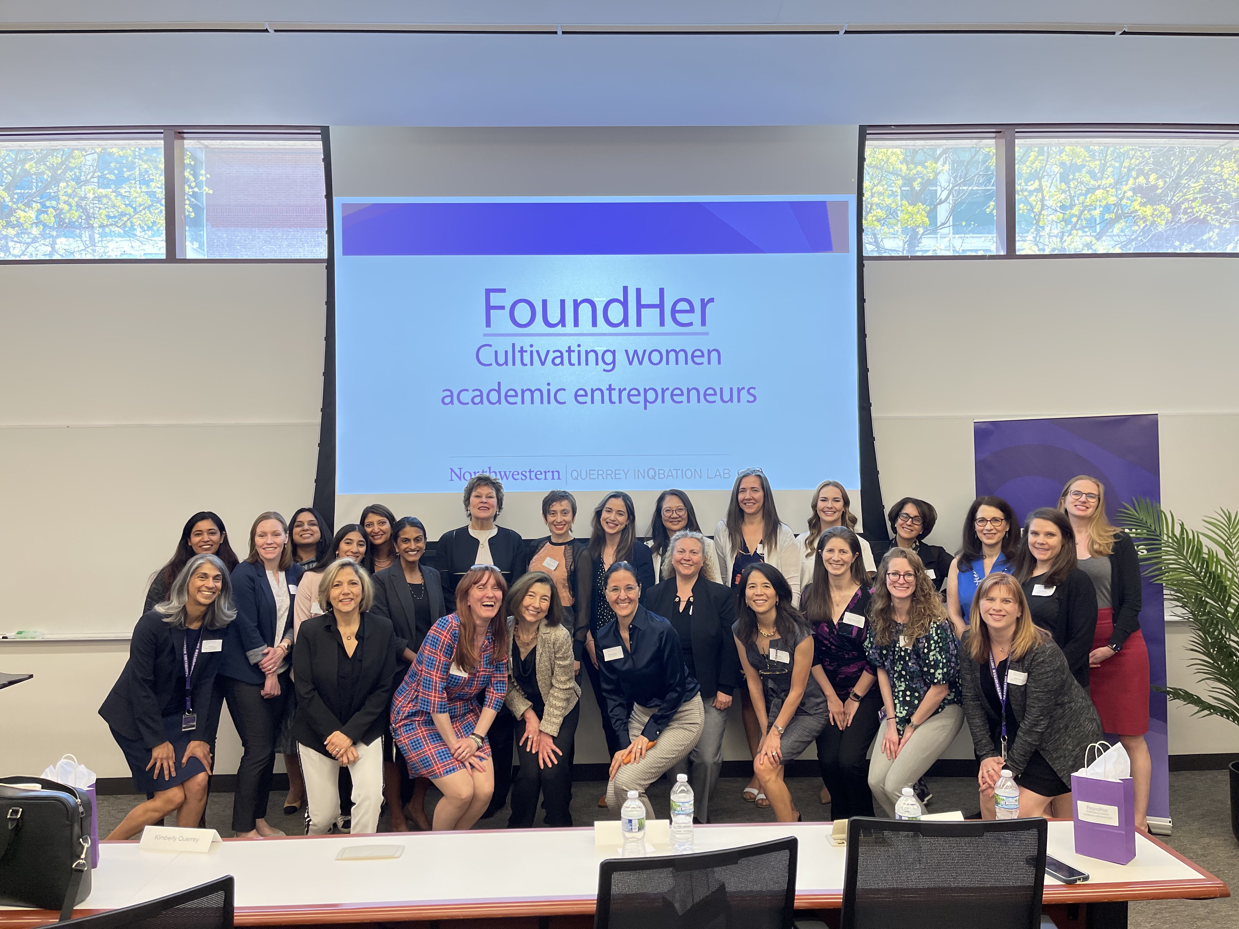 A group of women stand together in front of a screen reading: "FoundHer: Cultivating women academic entrepreneurs."